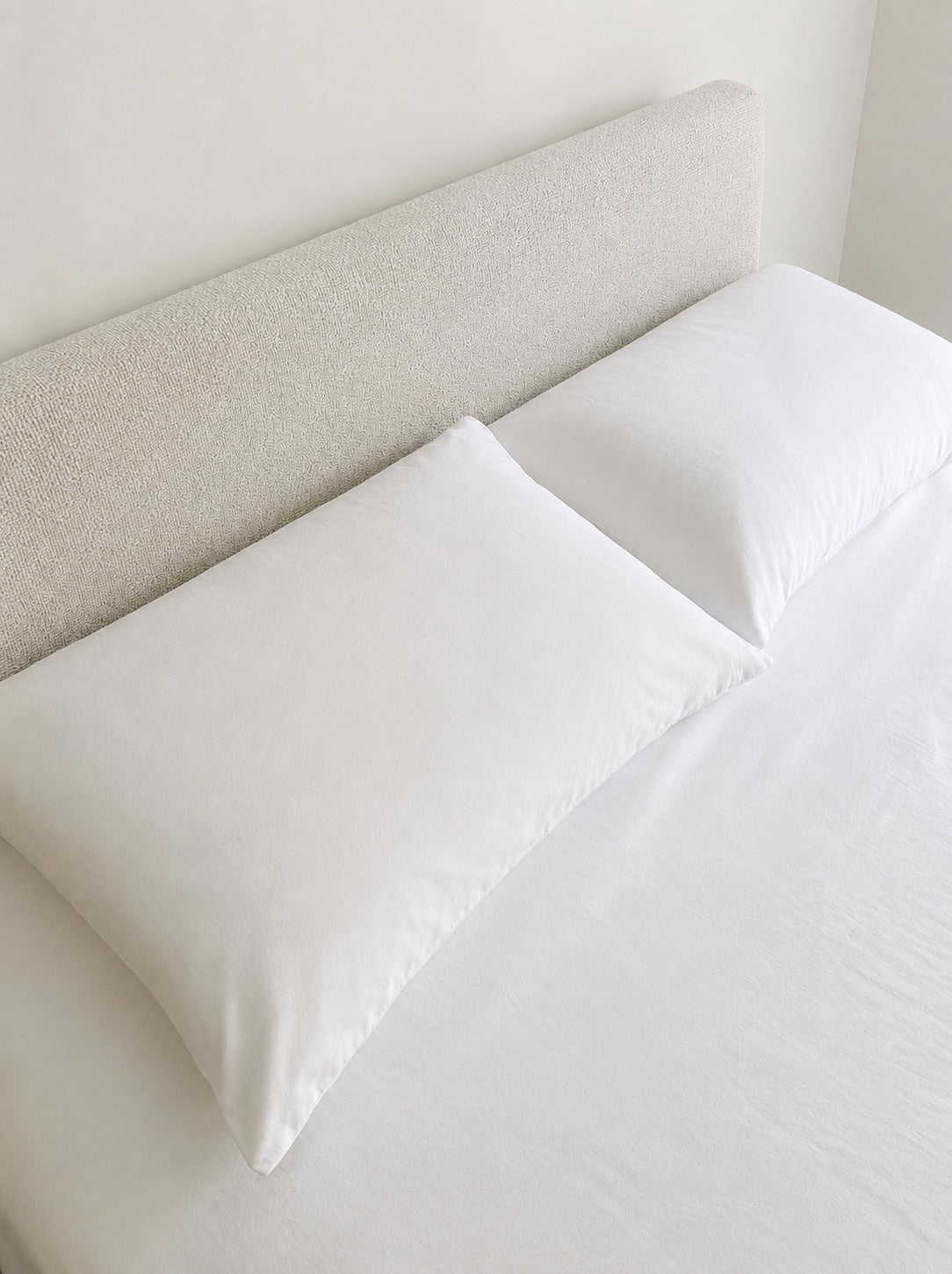 Bast & Co two pillowcases styled against a modern upholstered headboard